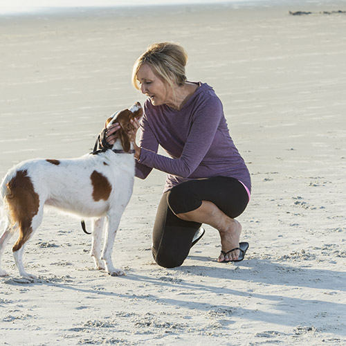 woman on beach kneeling and giving affection to rust spotted spaniel dog